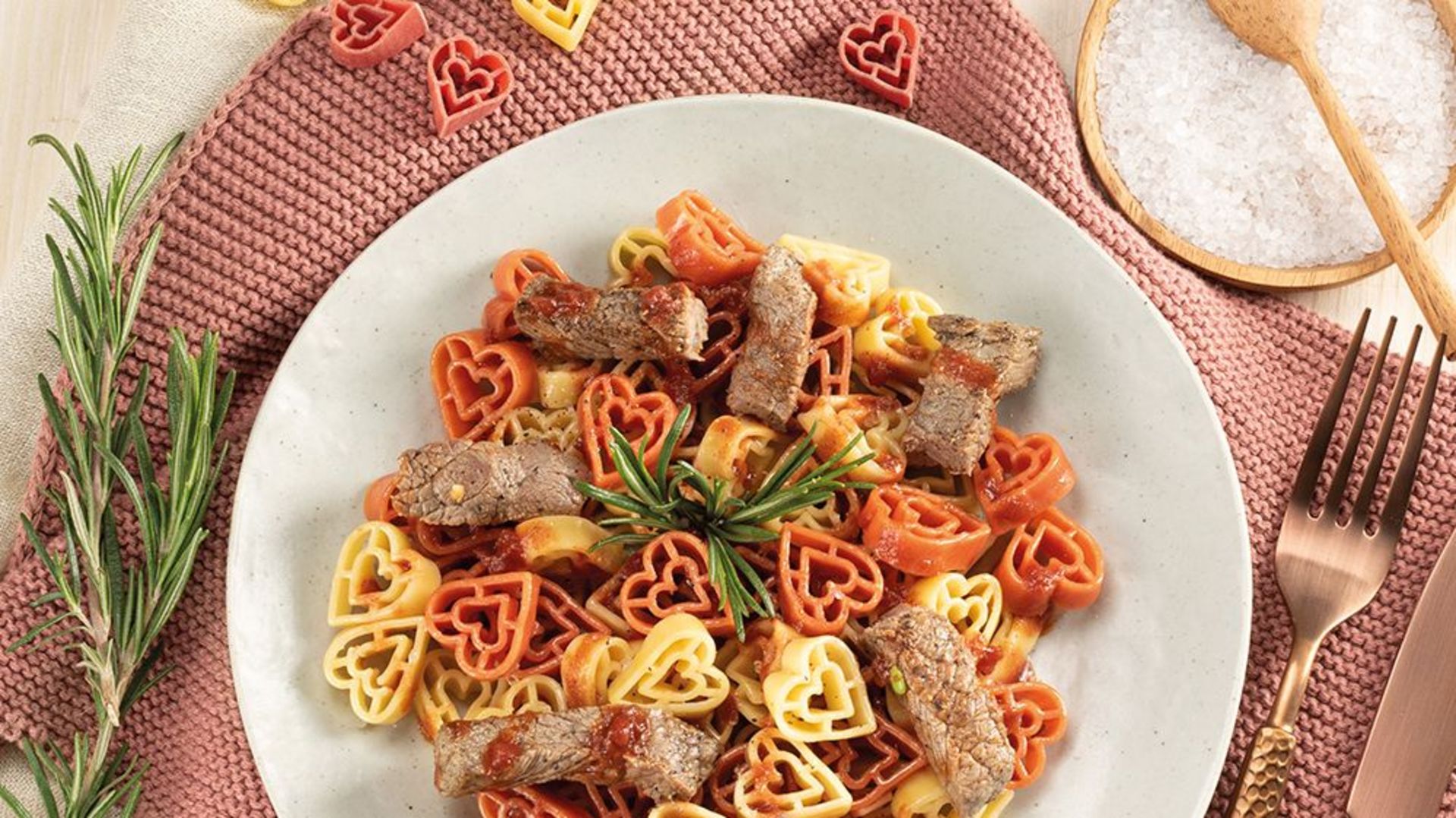 Teller mit Nudelherzen und Roastbeefstreifen in Tomaten-Rotwein-Sauce, garniert mit Rosmarin
