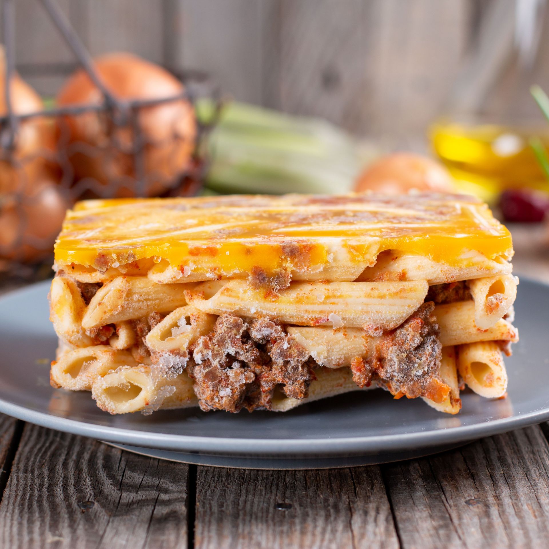 Plate of layered pasta bake with minced meat and cheese, served on a wooden table