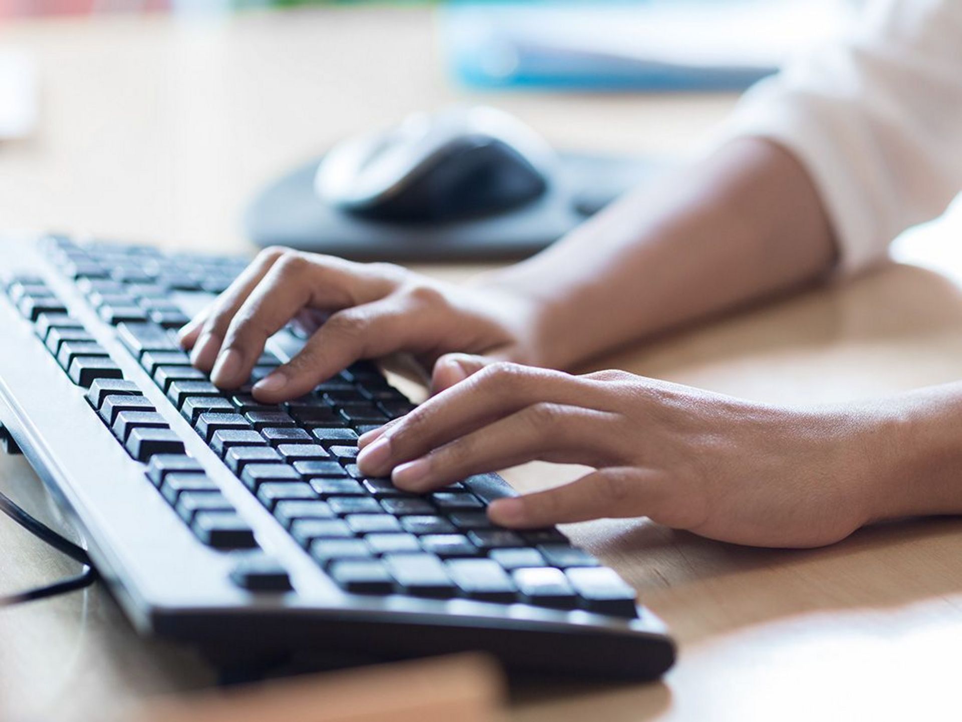 Hände tippen auf einer schwarzen Computertastatur auf einem Schreibtisch