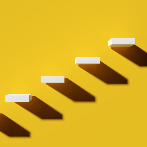 Weiße Treppenstufen mit Schatten auf gelbem Hintergrund, die einen Aufstieg symbolisieren