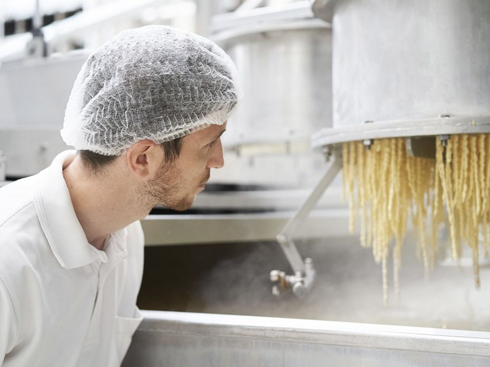 Produktionsmitarbeiter mit Haarnetz schaut auf eine Nudelmaschine in einer Produktionsanlage