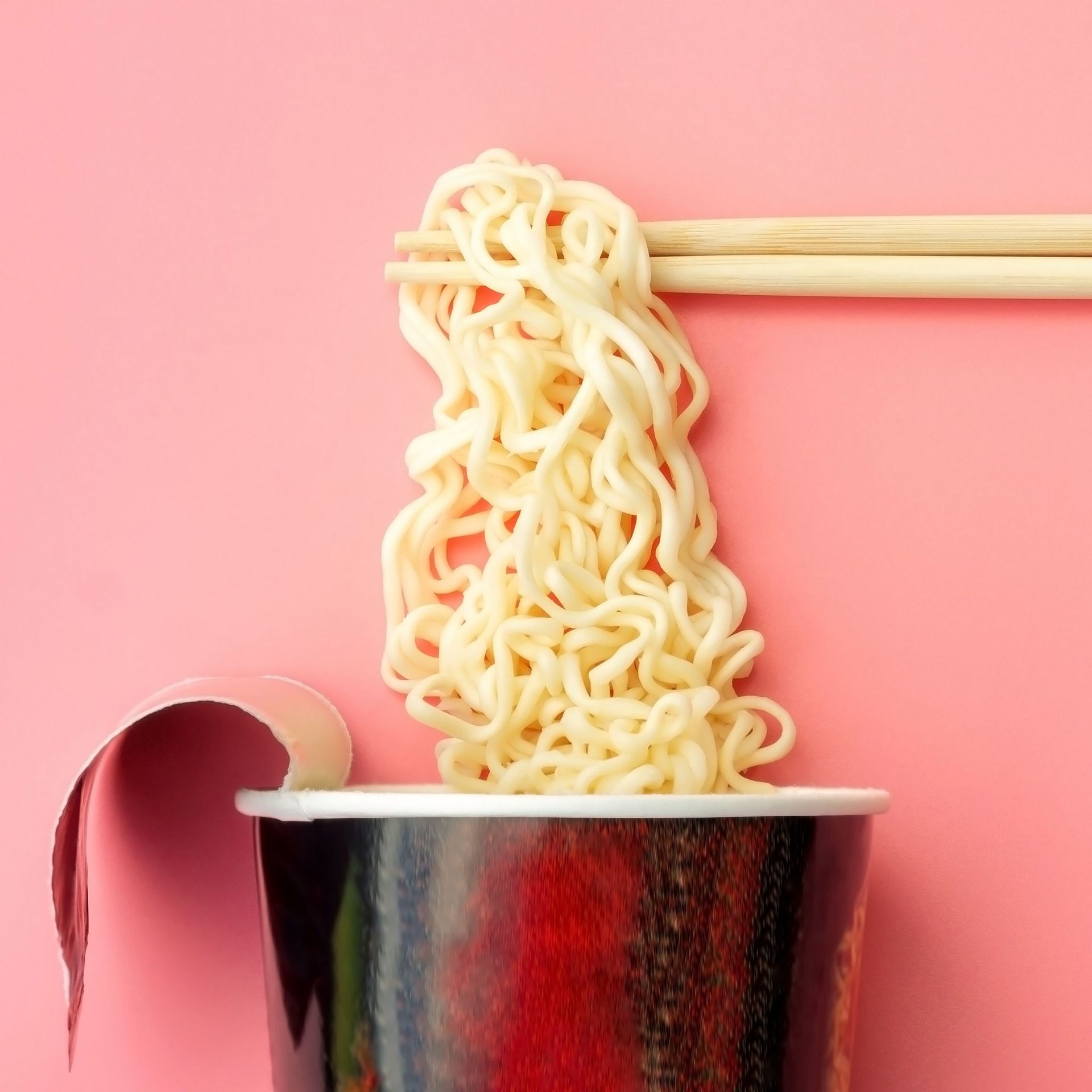 Instant cup with lifted, steaming instant noodles held by chopst