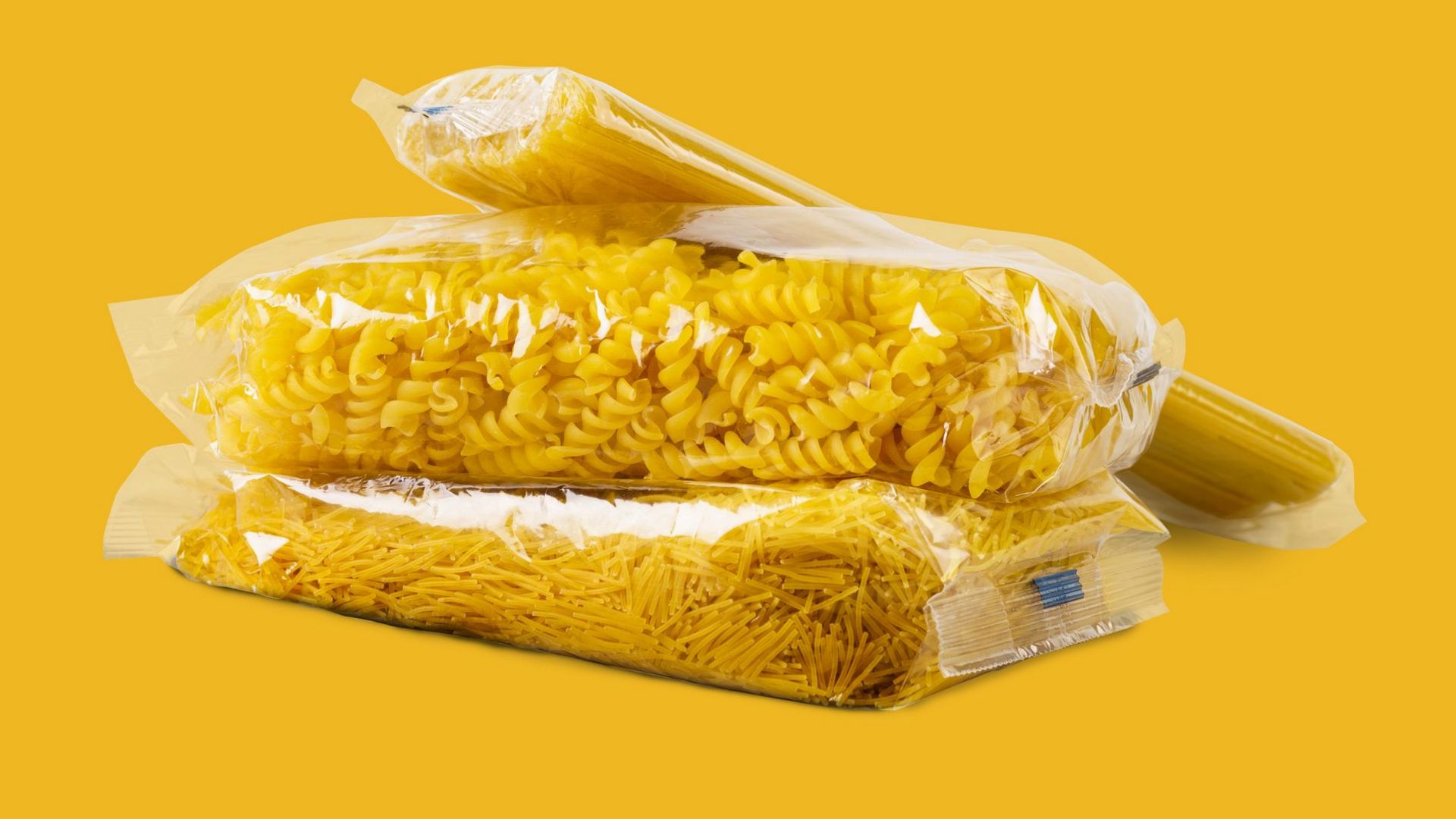 Mehrere Tüten Nudeln in einer durchsichtigen Verpackung auf gelbem Hintergrund.