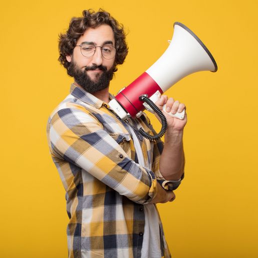 Mann mit Brille und kariertem Hemd hält ein Megafon vor gelbem Hintergrund